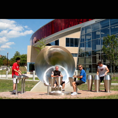 A place for communal music making adjacent to Ohio State University stadium. Individual components include: African Djembe drums mounted on seats around an Earth drum played with the feet; Afro-Cuban Conga, Quinto and Tumba drums; and Sun Drums based on Brazilian and Indonesian archetypes. Commissioned by the Ohio Percent for Art Program Fabrication: Eastern Sheet Metal l 